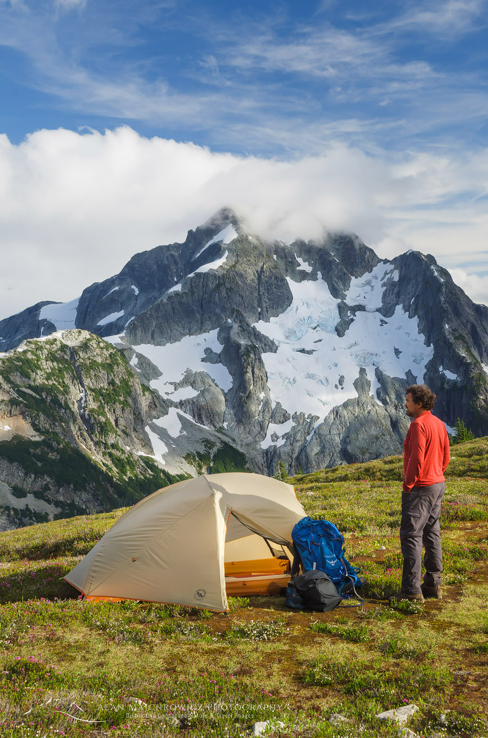 Adult male hiker in red shirt at backcountry camp on Red Face Mountain, Whatcom Peak seen in the distance. North Cascades National Park Washington #61584