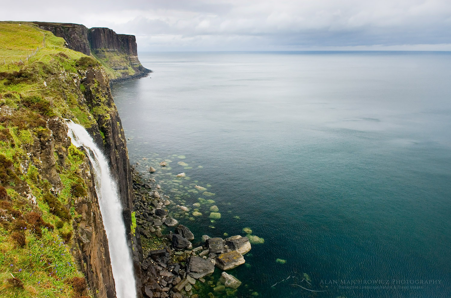Waterfall flowing over the cliffs of the coast of Isle of Skye Scotland, Kilt Rock is in the distance #11796
