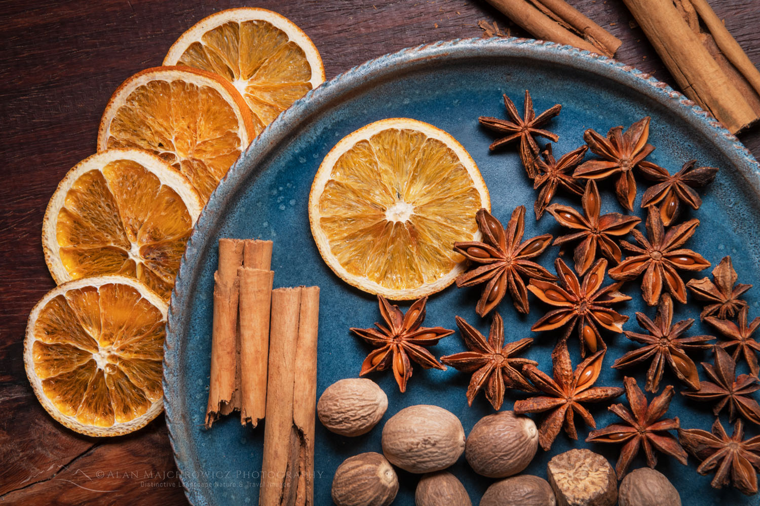 Spices and orange slices on blue stoneware plate, with cinnamon sticks, nutmeg, and star anise #79062