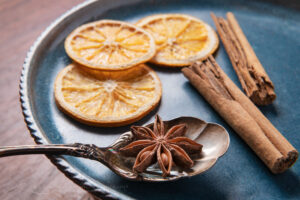Spices and dried orange slices on a blue stoneware plate, with cinnamon sticks, and star anise resting on an antique spoon #79064