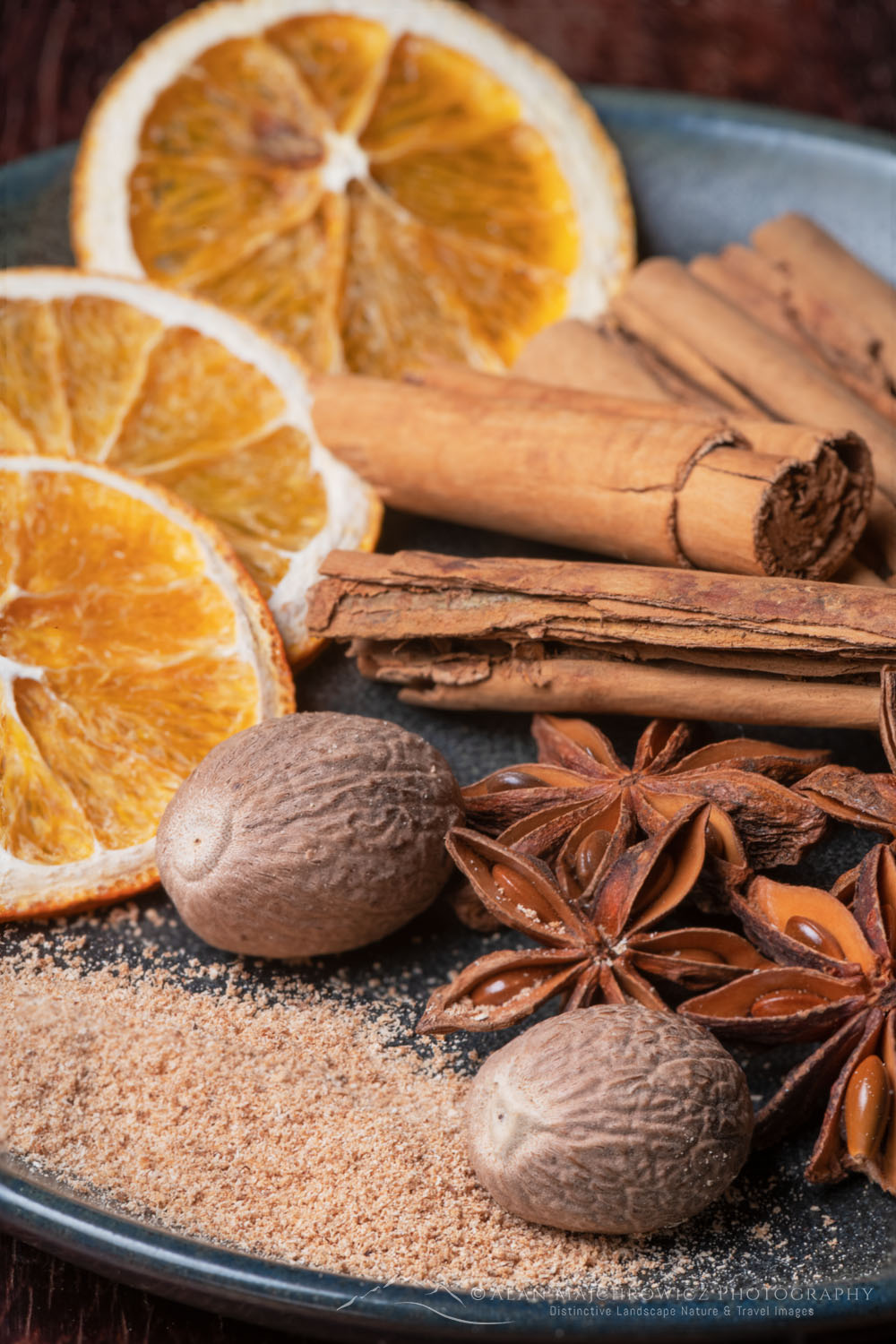 Spices and orange slices on stoneware plate, with cinnamon sticks, nutmeg, and star anise #79072