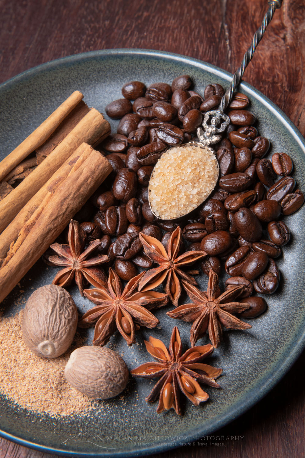 Spices, coffee beans, and orange slices on stoneware plate, with cinnamon sticks, nutmeg, star anise, and turbinado sugar on antique spoon #79081