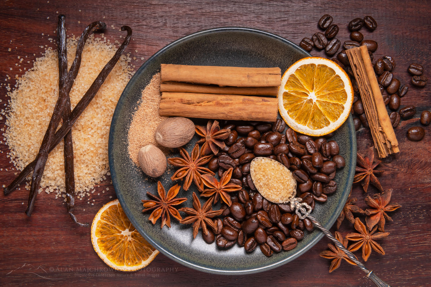 Spices, coffee beans, and orange slices on stoneware plate, with cinnamon sticks, vanilla bean, nutmeg, star anise, and turbinado sugar on antique spoon #79086