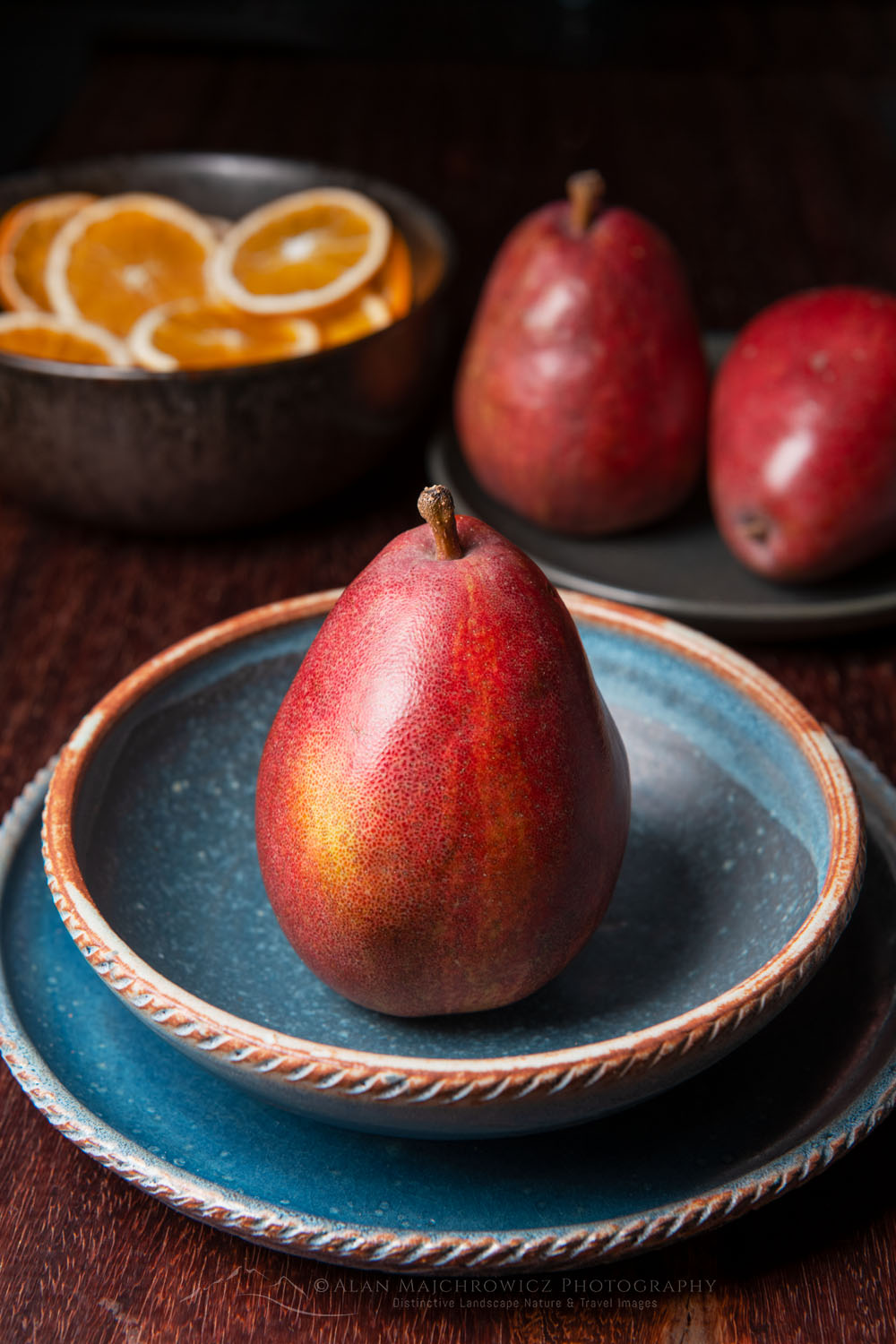 Red pear on blue stoneware bowl and plate, with dried orange slices in a bowl in the background #79089