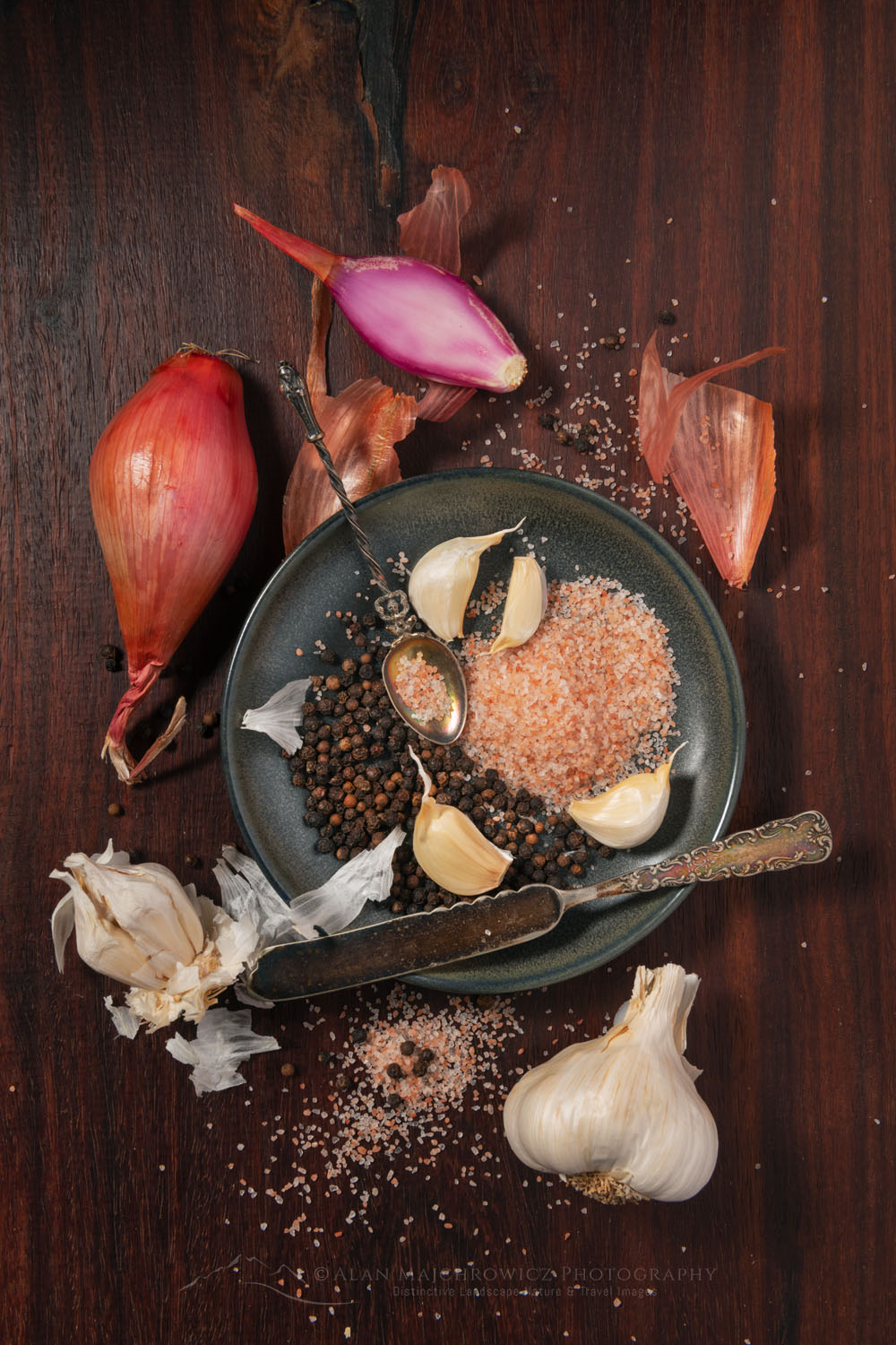 Culinary still life consisting of shallots, garlic, black peppercorns, and pink Himalayan sea salt with antique knife on a stoneware plate #78997