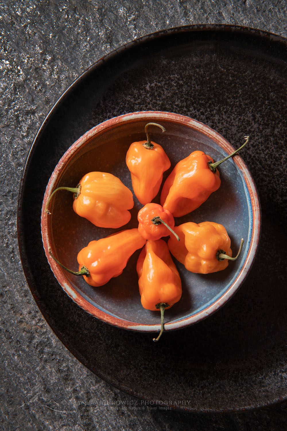 Arrangement of Habanero Chile peppers with stoneware bowl on stone backdrop #81237