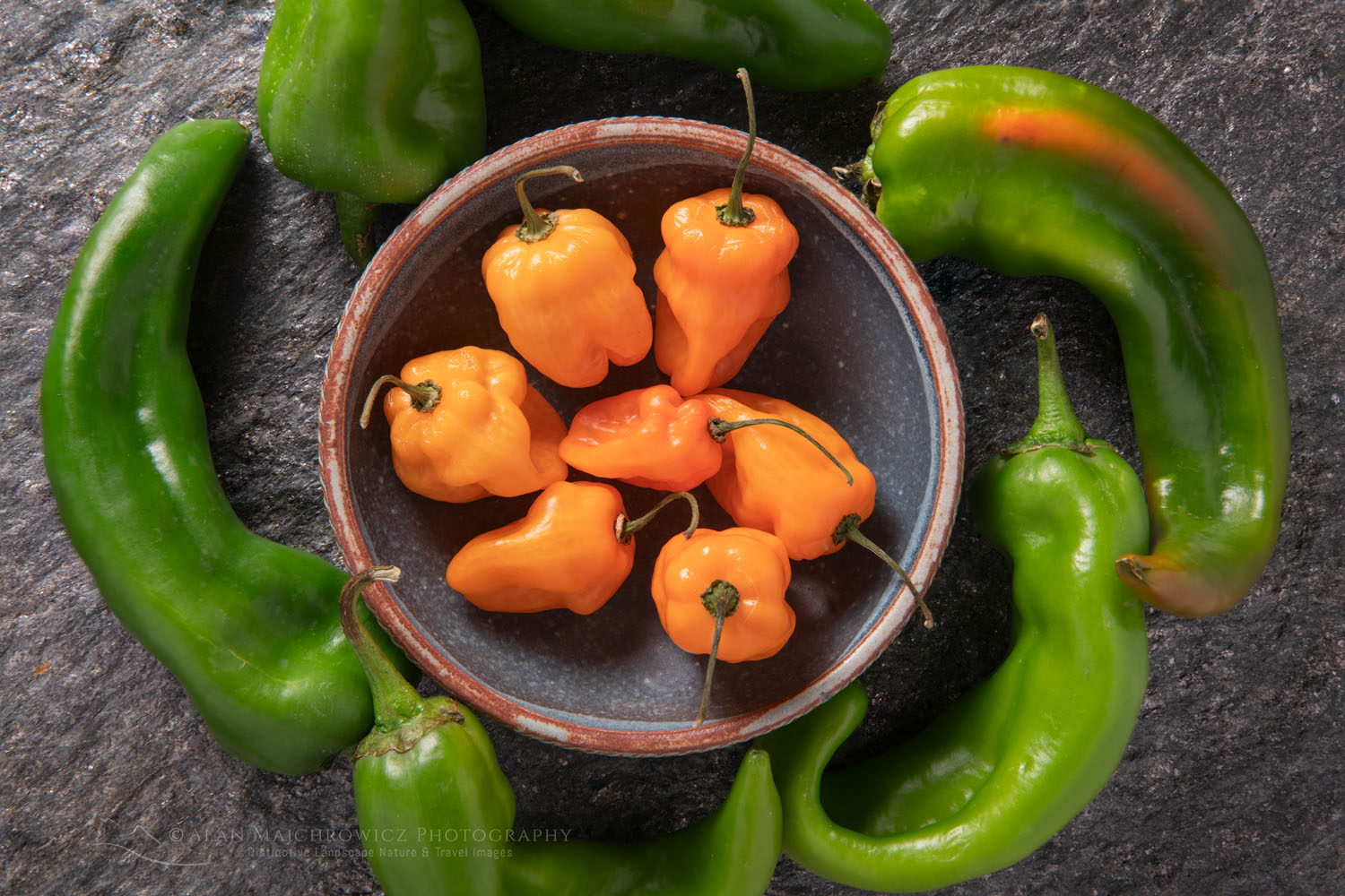 Arrangement of Habanero and Hatch Chile peppers with stoneware bowl on stone backdrop #81157