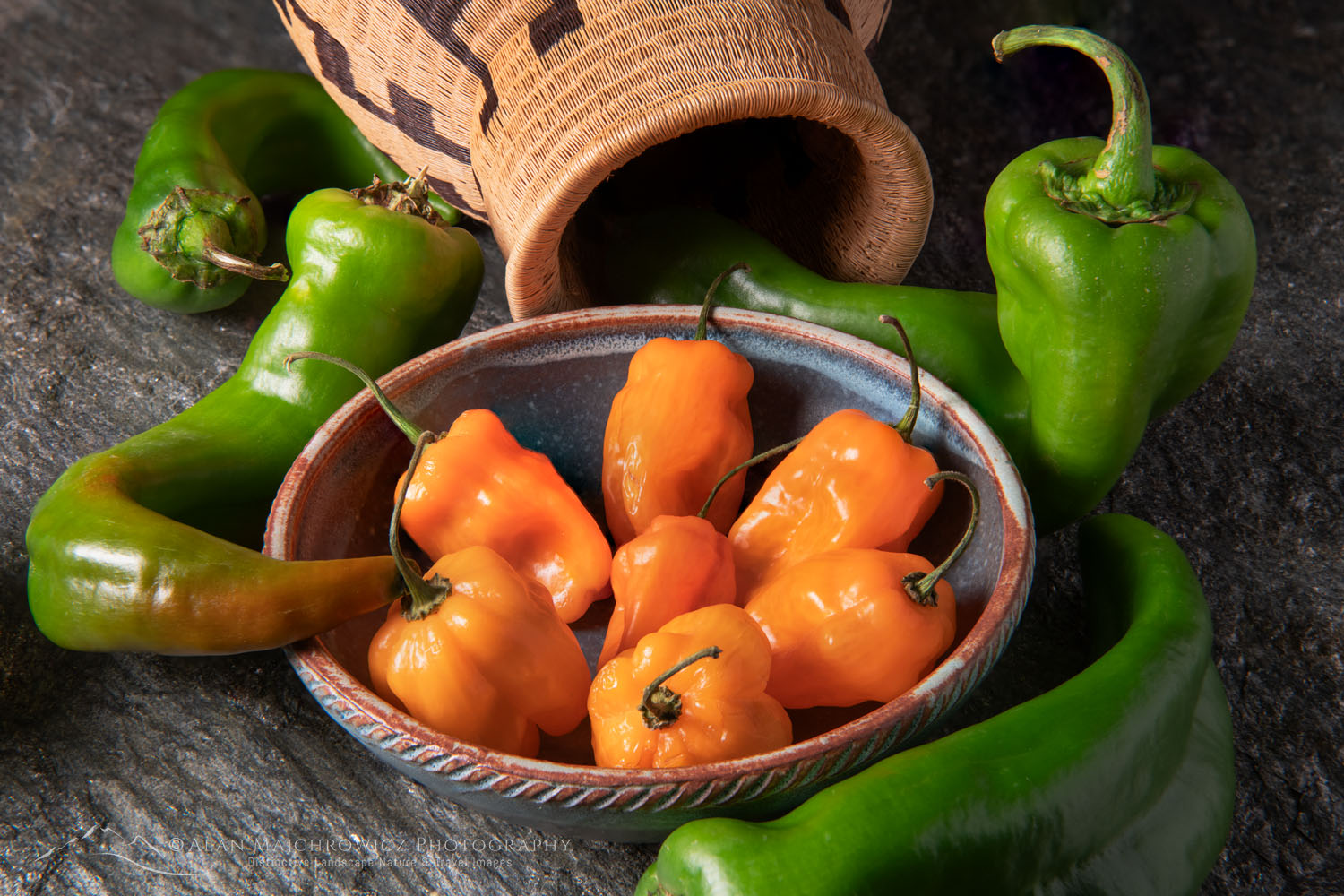 Arrangement of Habanero and Hatch Chile peppers with Panamanian Wounaan basket and stoneware bowl on stone backdrop #81160