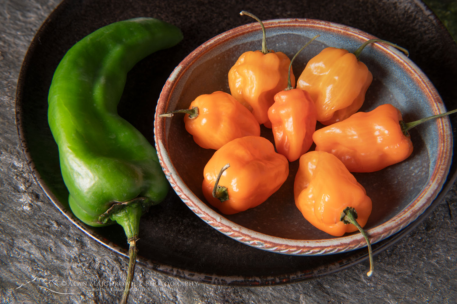 Arrangement of Habanero and Hatch chile peppers with stoneware bowl on stone backdrop #81193