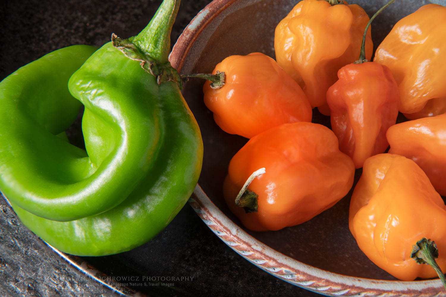 Arrangement of Habanero and Hatch chile peppers with stoneware bowl on stone backdrop #81200