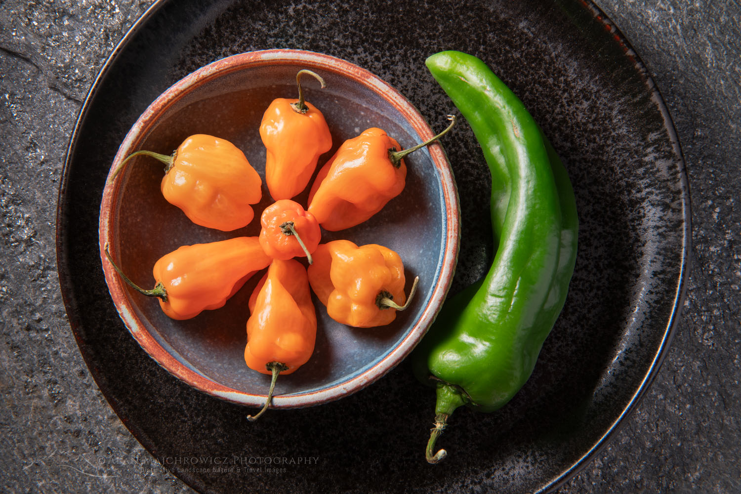 Arrangement of Habanero and Hatch chile peppers with stoneware bowl on stone backdrop #81240