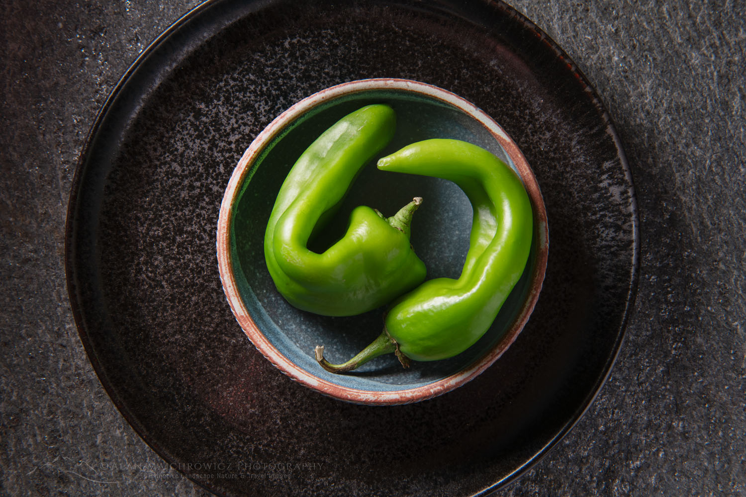 Arrangement of Hatch Chile peppers with stoneware bowl on stone backdrop #81230