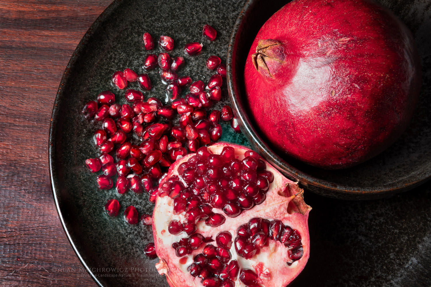 Pomegranates, segments, and seeds on black stoneware plate and bowl #81805