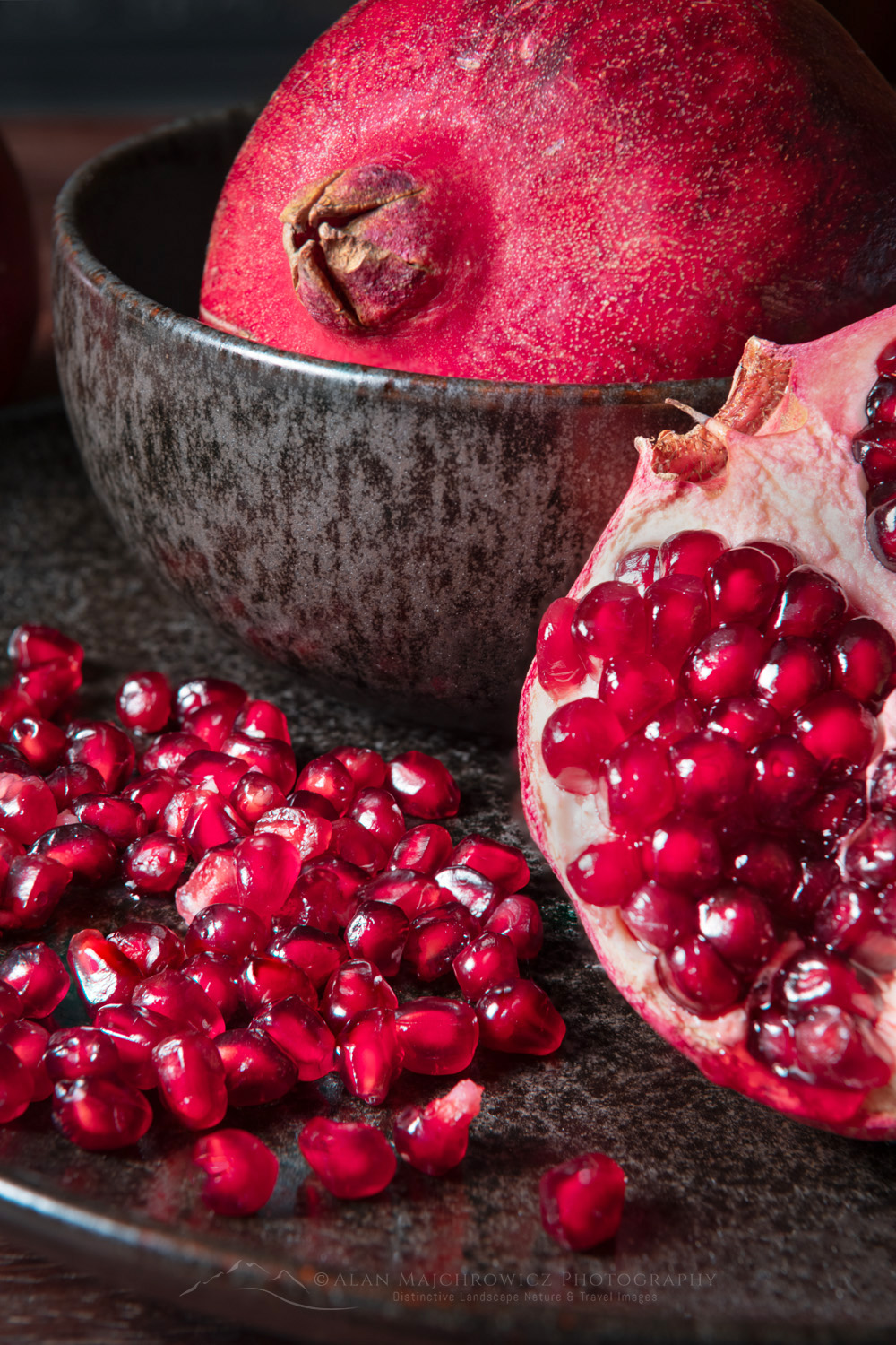 Pomegranates, segments, and seeds on black stoneware plate and bowl #81811