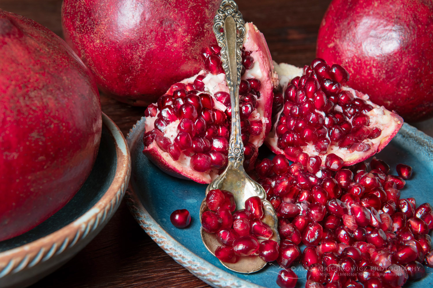 Pomegranates, segments, and seeds on blue stoneware plate and bowl with antique serving spoon #81836