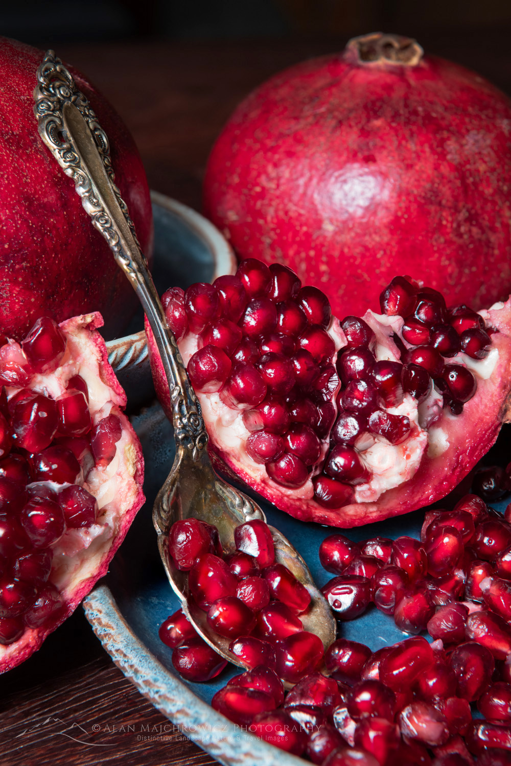 Pomegranates, segments, and seeds on blue stoneware plate and bowl with antique serving spoon #81859