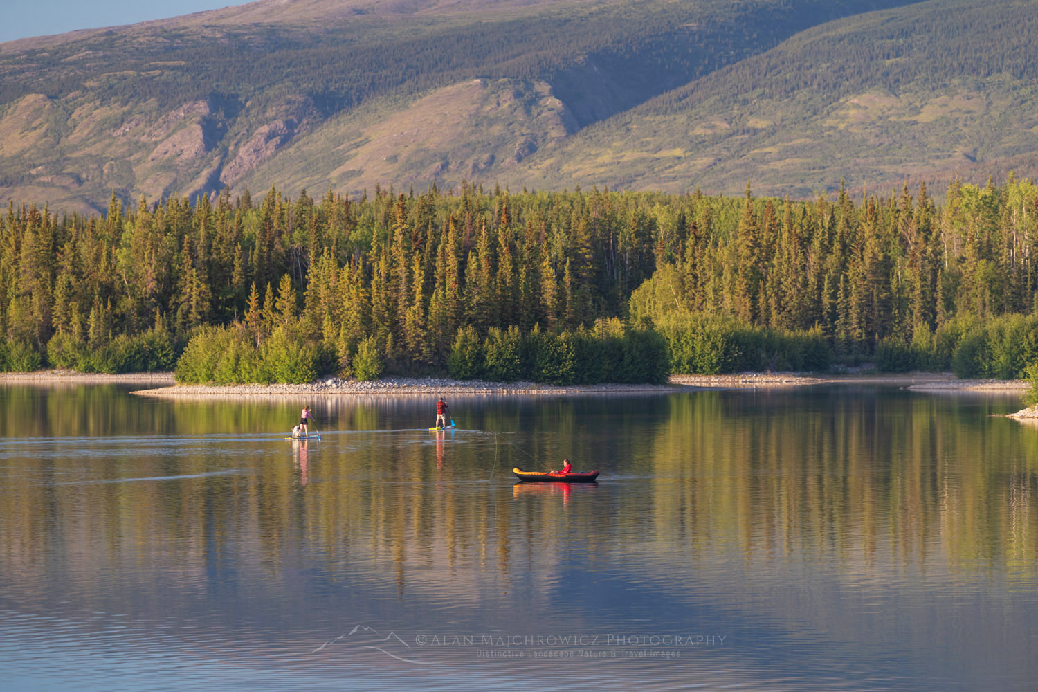 Two people on paddle boards and a man in a red raft fly fishing on Boya Lake. Tā Ch'ilā Park (Boya Lake Park), British Columbia #86933